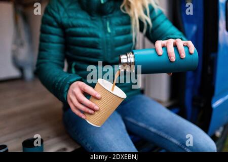 Donna di mezza età che versa il tè in una tazza monouso alla porta di camper Foto Stock