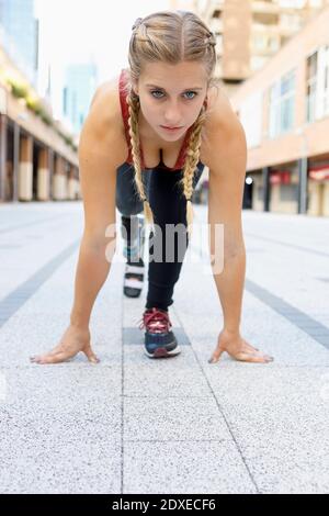 Giovane donna con gamba protesica accovacciata per la gara sportiva sentiero Foto Stock