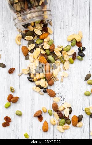 Vasetto di uvetta, arachidi, noci di anacardi, mandorle, soia, semi di girasole e semi di zucca versati su sfondo di legno Foto Stock