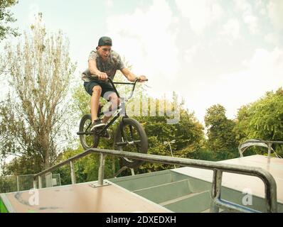 Giovane uomo che corre in bici BMX su salti al parco, Budapest, Ungheria. Foto Stock