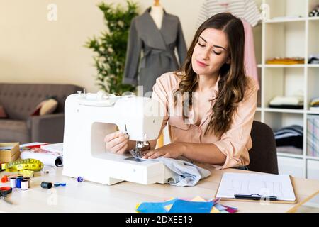Sorridente giovane donna creativa professionale utilizzando la macchina da cucire mentre si siede in studio Foto Stock