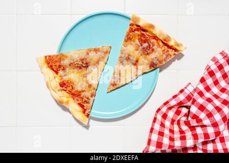 Due fette di pizza Margherita su piatto blu e rosso tovagliolo a scacchi Foto Stock