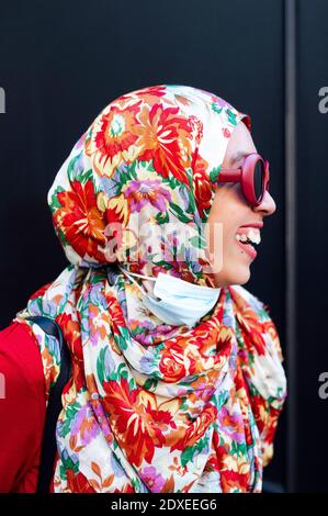 Donna allegra in hijab floreale contro parete nera durante COVID-19 Foto Stock