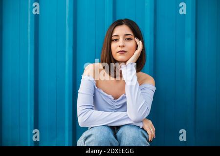 Giovane bella donna seduta contro parete blu Foto Stock