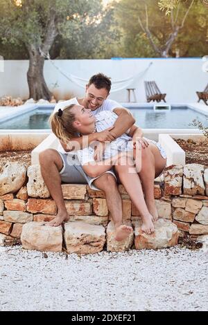 Felice giovane coppia che si guarda l'un l'altro mentre si siede contro piscina nel cortile Foto Stock