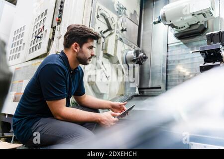 Lavoratore maschile che analizza le macchine mentre tiene il tablet digitale in fabbrica Foto Stock