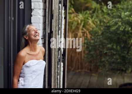 Donna giovane allegra che indossa un asciugamano in piedi alla porta della casa Foto Stock