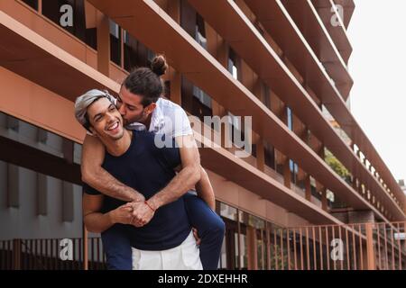 Uomo piggybacking gay partner mentre guardando lontano contro la costruzione in città Foto Stock