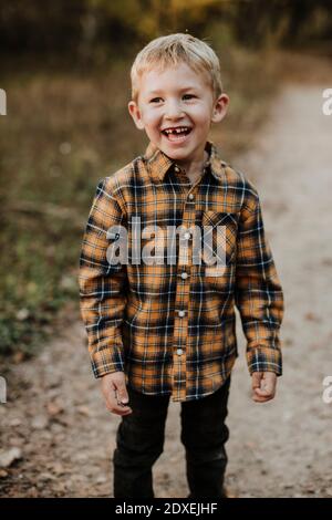 Ragazzo sorridente che indossa una camicia in plaid in piedi sul sentiero nella foresta Foto Stock
