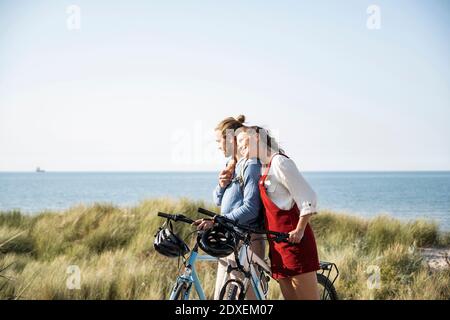 Giovane donna appoggiata sull'uomo mentre sta in piedi con le biciclette a. spiaggia Foto Stock