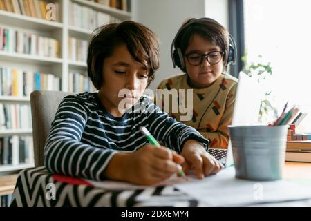 Ragazzo che scrive note mentre l'amico maschio è seduto accanto a lui casa Foto Stock