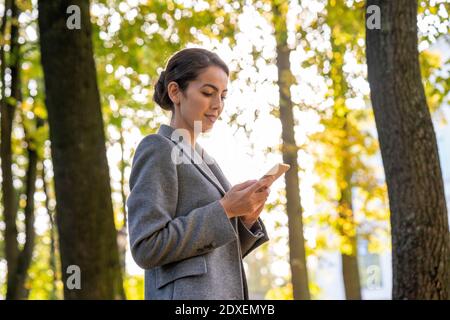 Messaggi di testo per uomo d'affari su smartphone mentre si è in piedi in parcheggio durante l'autunno Foto Stock