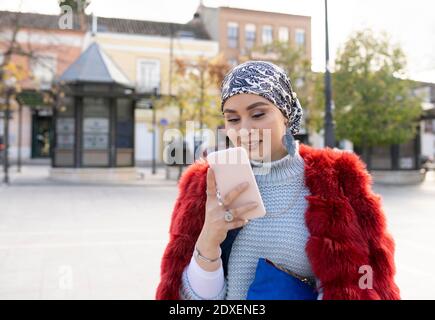 Giovane donna che indossa abiti caldi utilizzando il telefono cellulare mentre si è in piedi in città Foto Stock