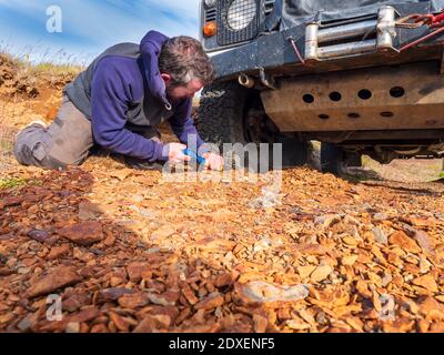 Viaggiatore maschile cercando di pneumatico libero di auto bloccato nel mezzo della strada rocciosa, Islanda Foto Stock