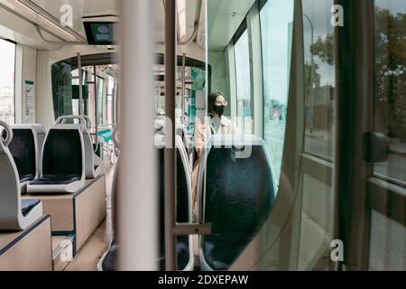 Donna che indossa una maschera mentre si è seduti in tram Foto Stock