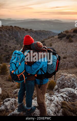 La coppia si abbraccia mentre si alza sulla vetta della montagna durante il tramonto Foto Stock