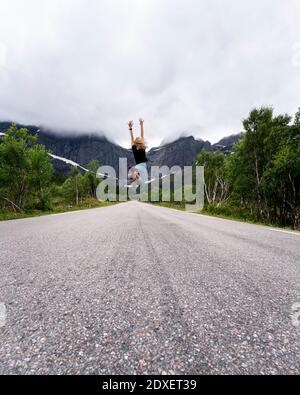 Donna con saltando a mano su strada contro la montagna a Lofoten, Norvegia Foto Stock