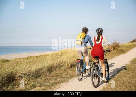 Giovane coppia che indossa un casco da bicicletta che corre in bicicletta contro il cielo limpido Foto Stock