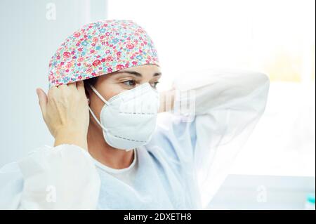 Donna dentista professionista indossare maschera protettiva mentre si è in piedi Clinica durante Covid-19 Foto Stock