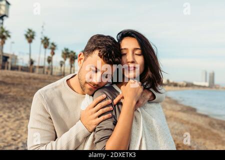 Fidanzato abbracciando la ragazza contro il cielo in spiaggia Foto Stock