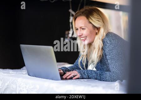 Donna felice che lavora su un computer portatile mentre si sdraiava sul letto camper Foto Stock