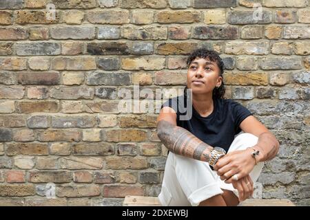 Donna premurosa che guarda via mentre si siede contro muro di mattoni a. cortile posteriore Foto Stock