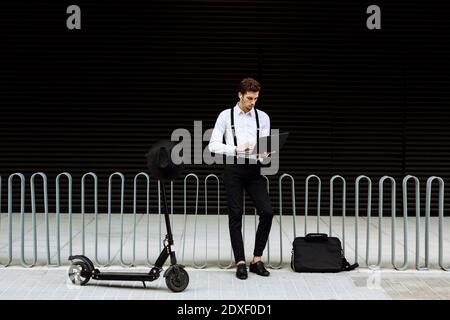 Uomo d'affari alla moda che lavora su un computer portatile in città Foto Stock