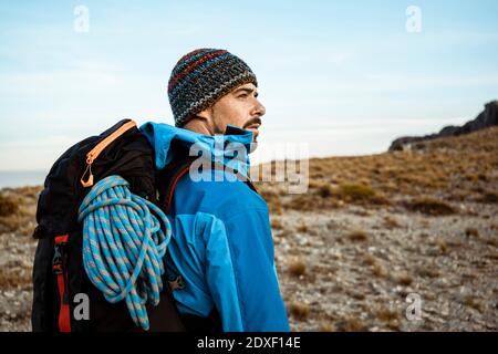 Pensieroso escursionista maschile guardando via mentre si sta in piedi sulla montagna contro cielo Foto Stock
