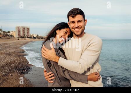 Ragazza sorridente e fidanzato si abbracciano contro il cielo a. spiaggia Foto Stock