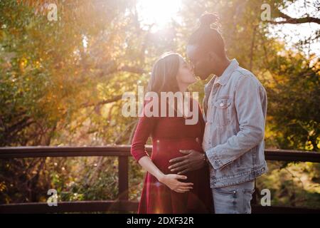 Donna incinta e uomo che baciano mentre si trova in parcheggio Foto Stock