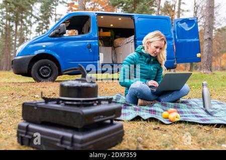 Donna che lavora su un computer portatile mentre si siede su coperta da picnic a. Inseguimento di Cannock Foto Stock