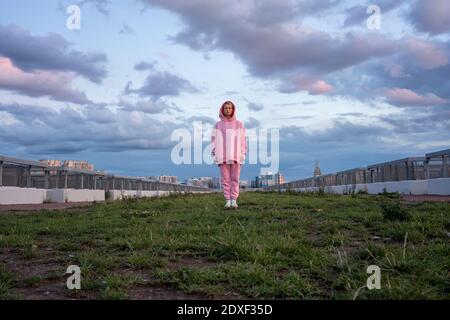 Ritratto di giovane donna con capelli rosa con camicia con cappuccio rosa in piedi su erba Foto Stock