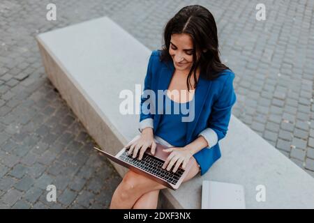 Donna d'affari che usa il computer portatile mentre si siede sulla panca Foto Stock