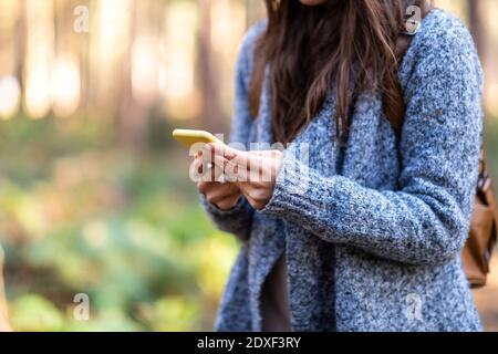 Donna che tiene lo smartphone mentre si trova nella foresta di Cannock Chase Foto Stock