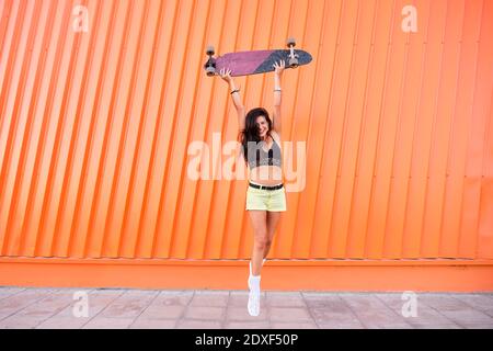 Ritratto di giovane donna in piedi di fronte al ferro ondulato parete con longboard in mani Foto Stock