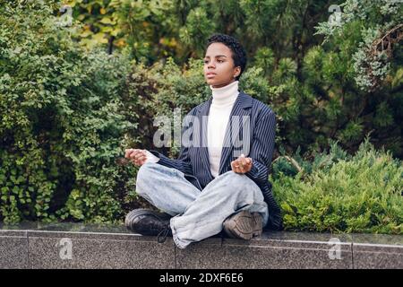 Giovane donna d'affari premurosa che guarda via mentre pratica yoga sul trattenere parete Foto Stock