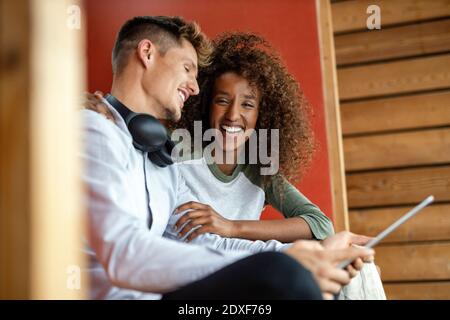 Uomo felice con tablet digitale seduto da donna allegra a. casa Foto Stock