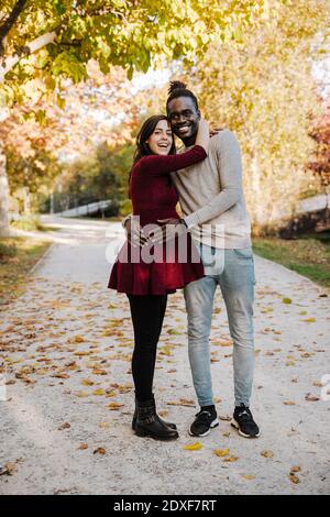 Donna incinta felice abbracciando l'uomo mentre si trova sul sentiero dentro parcheggio Foto Stock