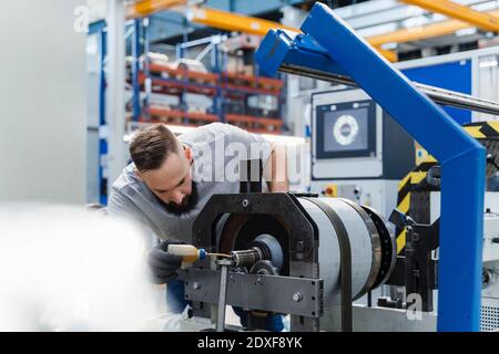 Tecnico di sesso maschile macchinari di lubrificazione durante l'esame in industria Foto Stock