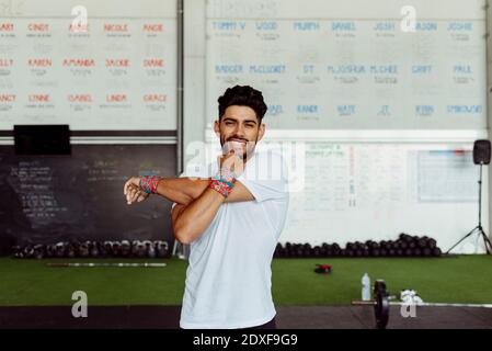 Giovane uomo sorridente mentre si allunga la mano in palestra Foto Stock