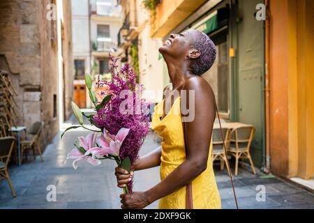 Donna allegra con fiori in piedi accanto al bar in città Foto Stock