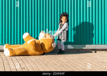 Ragazza che trascina orsacchiotto sul sentiero mentre si gioca contro il verde parete Foto Stock