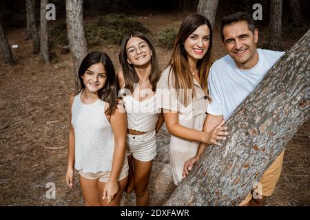 Una famiglia sorridente che si trova dietro il tronco d'albero nella foresta Foto Stock