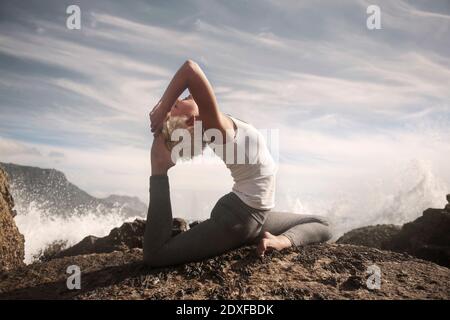 Donna flessibile che pratica Sirsapada Natarajasana sulla formazione rocciosa Foto Stock