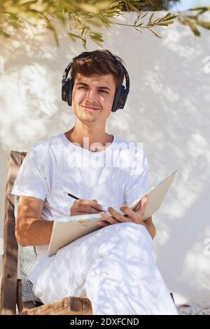Sorridendo l'uomo che pensa mentre ascolta la musica contro la parete bianca nel cortile posteriore Foto Stock