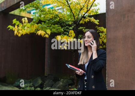 Sorridente imprenditore femminile che parla al telefono mentre si è in piedi di marrone parete Foto Stock