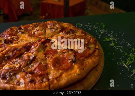 Gustosi pepperoni pizza e ingredienti per cucinare pomodori basilico su fondo di legno nero. Vista dall'alto della pizza con peperoni caldi. Foto Stock