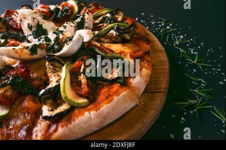 Gustosa pizza ratatouille e ingredienti per cucinare pomodori zucchini arrosto, formaggio fresco al basilico su sfondo di legno nero. Vista dall'alto della pizza calda. W Foto Stock