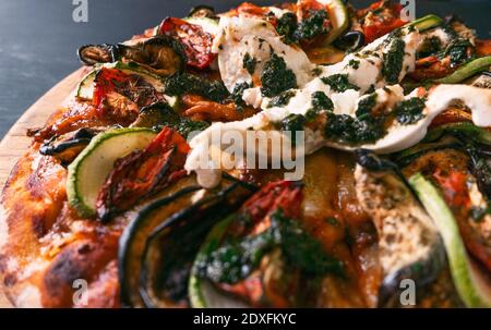 Gustosa pizza ratatouille e ingredienti per cucinare pomodori zucchini arrosto, formaggio fresco al basilico su sfondo di legno nero. Vista dall'alto della pizza calda. W Foto Stock