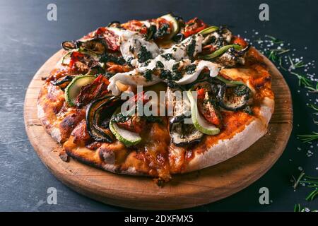 Gustosa pizza ratatouille e ingredienti per cucinare pomodori zucchini arrosto, formaggio fresco al basilico su sfondo di legno nero. Vista dall'alto della pizza calda. W Foto Stock